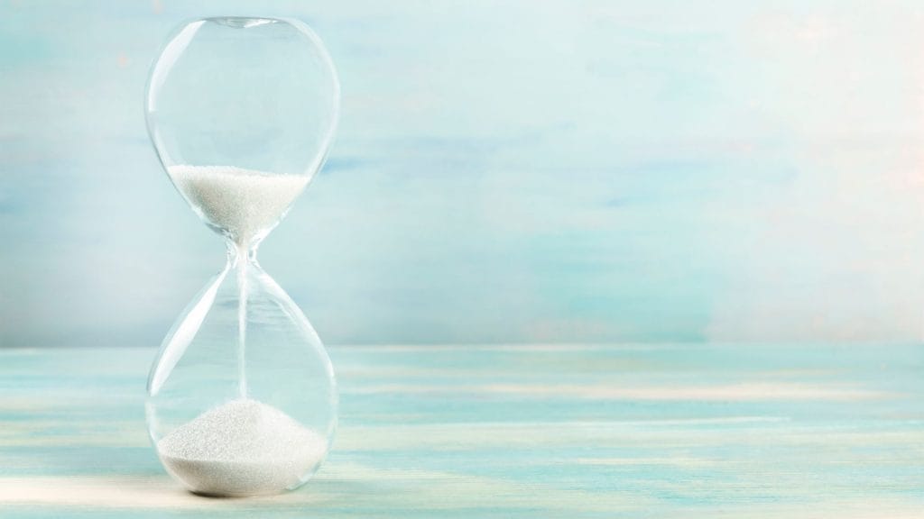 A clear glass hourglass with white sand flowing, symbolising taking a short mindful pause.