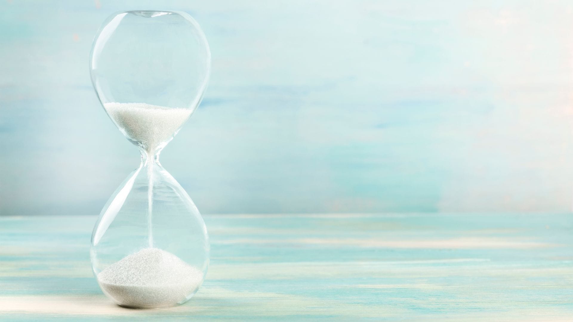 A clear glass hourglass with white sand flowing, symbolising taking a short mindful pause.