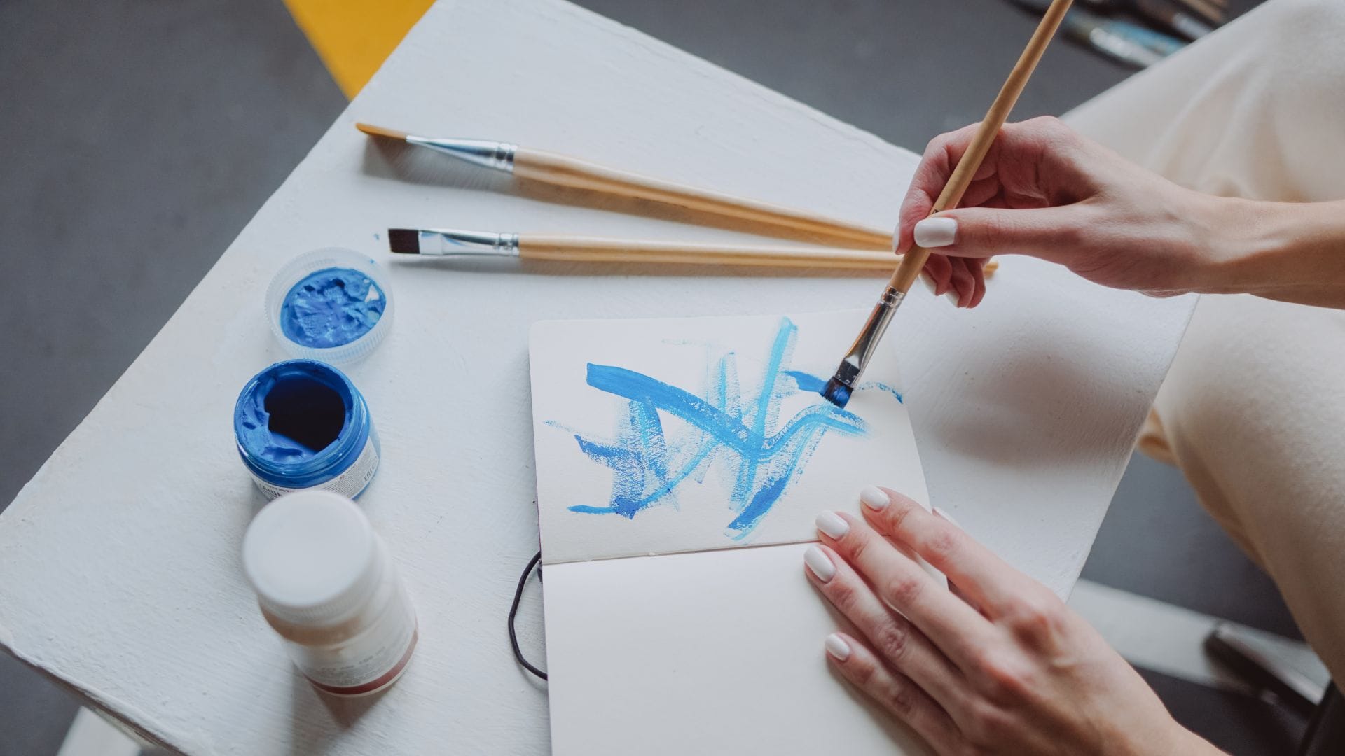 Hands painting calm blue brushstrokes in a sketchbook as a mindful art ritual.