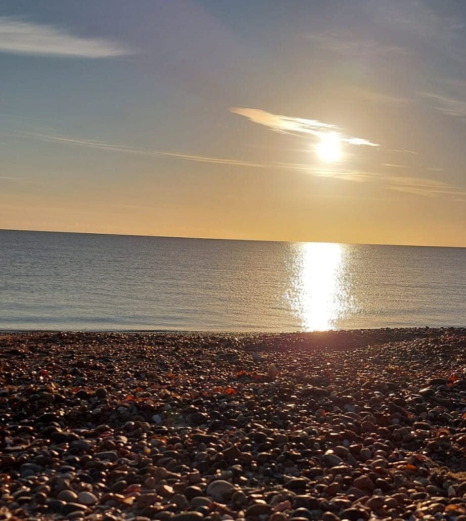 Sunlight reflecting on calm sea waves at sunset, viewed from a pebble beach.