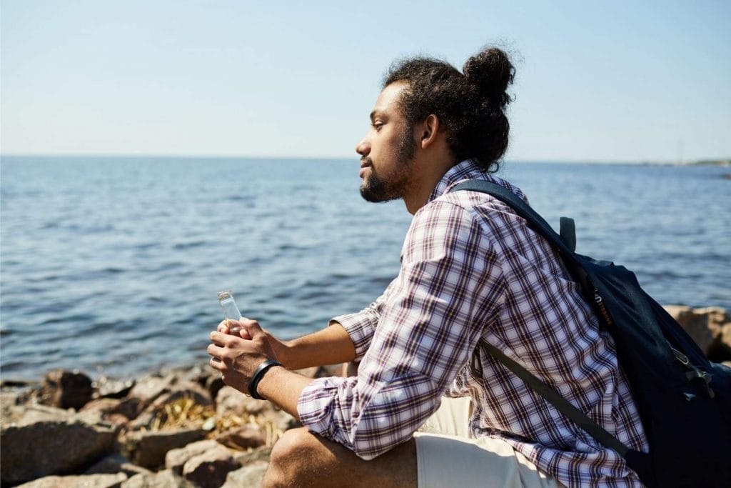 Man sitting by the sea, looking thoughtfully at the horizon, representing mindfulness and calm reflection.