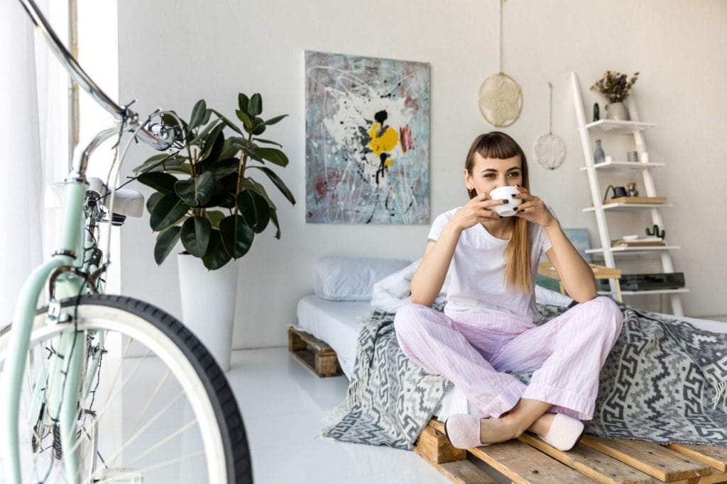 Woman sitting cross-legged in a bright, calm room, drinking tea and enjoying a quiet mindful moment.
